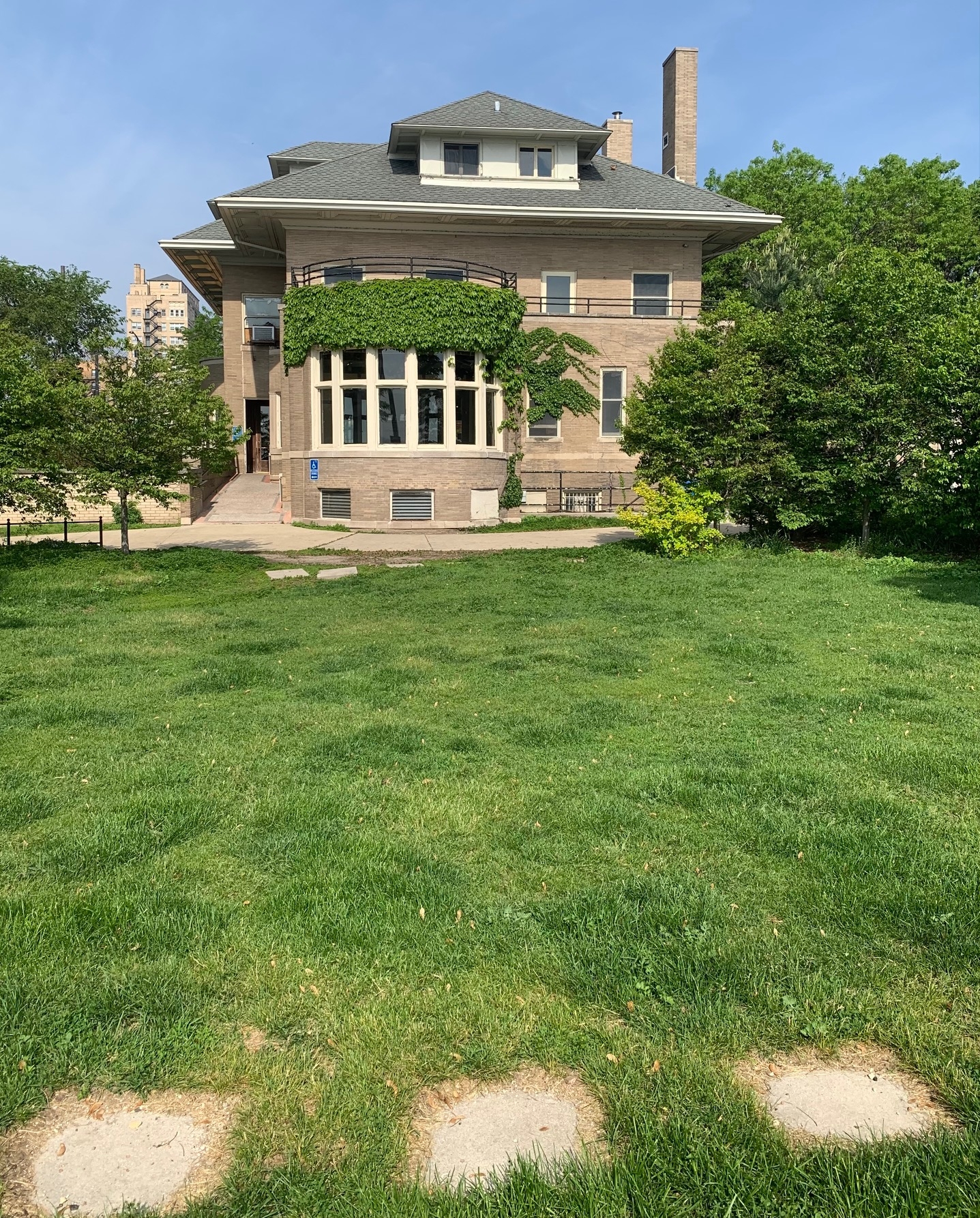Large brick house with ivy-covered rounded front section, situated across a green lawn with stepping stones.